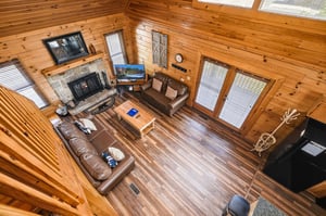 Youll love gathering in this open living space with warm wood beams, a crackling stone fireplace, cozy leather seating, and natural light streaming through windows framing serene outdoor views.