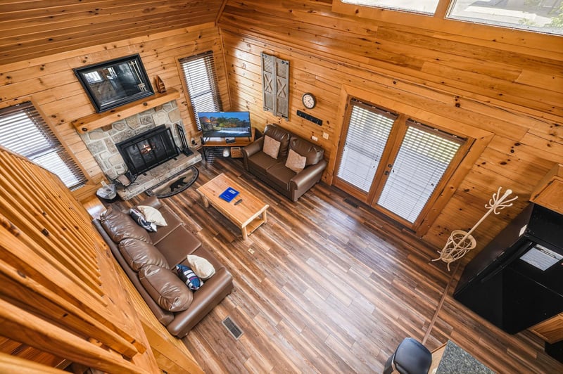 Youll love gathering in this open living space with warm wood beams, a crackling stone fireplace, cozy leather seating, and natural light streaming through windows framing serene outdoor views.