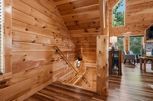 Step into your cozy cabin retreat, where warm knotty pine walls and soaring ceilings create an inviting atmosphere. Natural light streams through tall windows, highlighting the rustic charm throughout