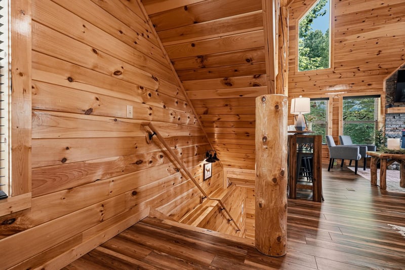 Step into your cozy cabin retreat, where warm knotty pine walls and soaring ceilings create an inviting atmosphere. Natural light streams through tall windows, highlighting the rustic charm throughout