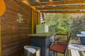 Your private covered deck offers the perfect outdoor entertaining space with a bar setup and BBQ grill surrounded by peaceful forest views.