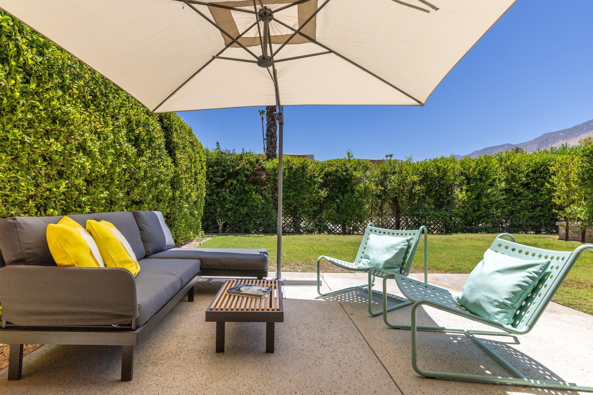 Back patio located off of the living room and primary bedroom featuring a table and chairs for morning coffee, umbrella, and ample outdoor seating.