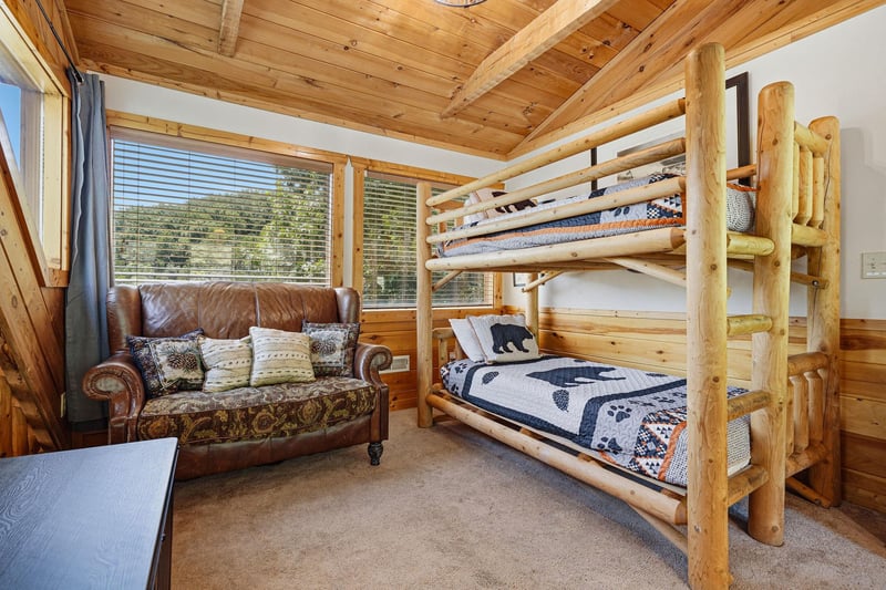 Your cozy rustic bedroom features handcrafted log bunk beds and warm woodpaneled walls and ceilings, creating a charming mountain retreat perfect for family adventures.