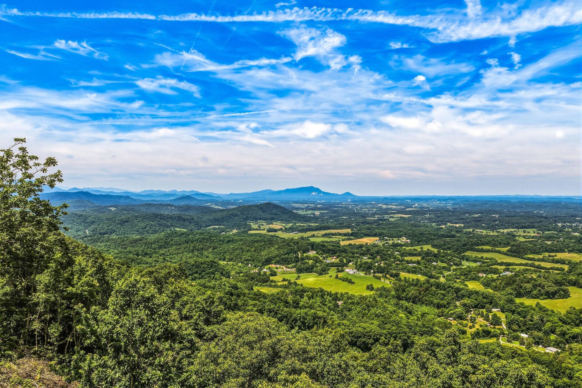 Expansive mountain and valley vistas stretch across lush green forests and rolling farmland beneath a brilliant blue sky, showcasing the propertys scenic surroundings.