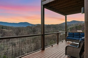 Covered mountain terrace showcases stunning sunset views over forested peaks and valley below.