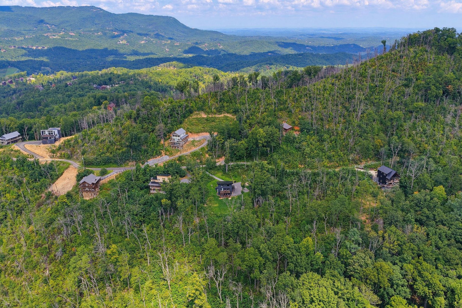 Aerial view of a secluded mountain retreat showcasing individual cabins nestled among lush forest, with sweeping views of the surrounding Blue Ridge Mountains and valleys.