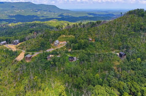 Aerial view of a secluded mountain retreat showcasing individual cabins nestled among lush forest, with sweeping views of the surrounding Blue Ridge Mountains and valleys.