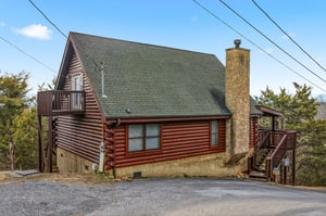 Rustic log cabin with stone chimney nestled among trees, featuring wooden decks and peaceful mountain surroundings for your getaway.