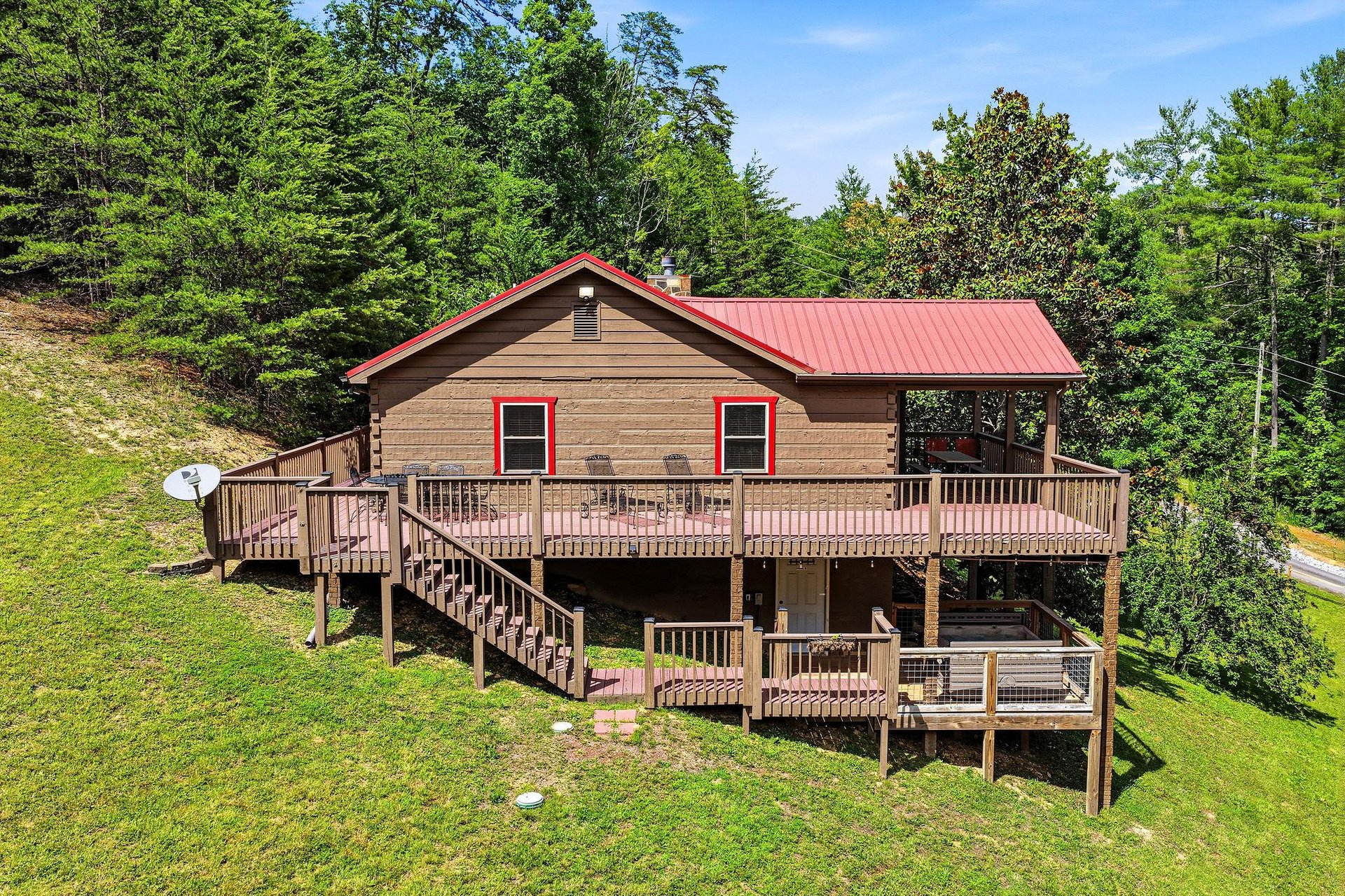 A charming cabinstyle property nestled in lush greenery, featuring a red metal roof and spacious wraparound decks perfect for mountain retreats.