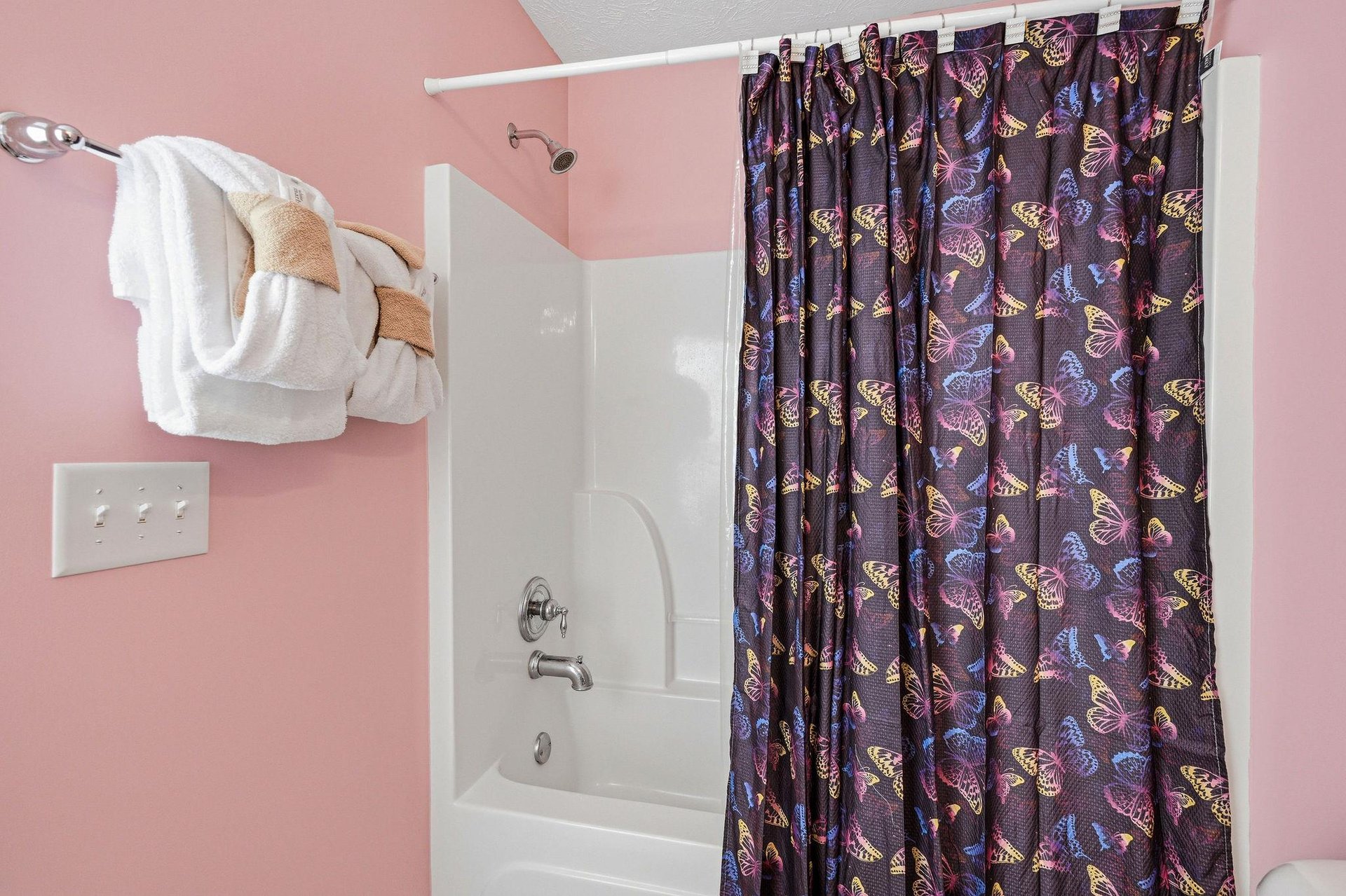 Refresh in your private bathroom with a whimsical butterflypatterned shower curtain and soft pink walls that create a cheerful, welcoming atmosphere.