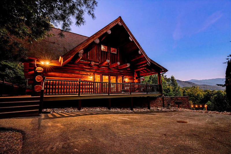 A beautiful log cabin property set among natural surroundings with mountain vistas in the distance, captured at twilight with warm lighting highlighting the handcrafted timber construction.