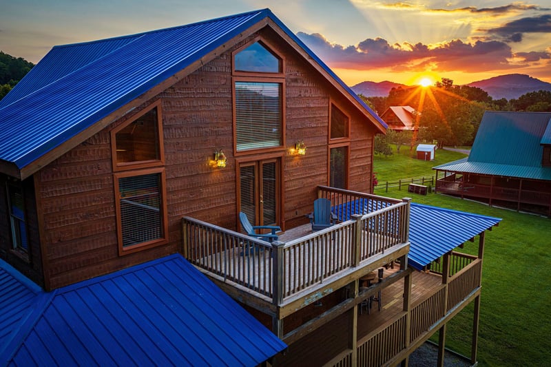 A stunning mountain view from the property with a vibrant sunset illuminating the landscape. The rustic cabin features a spacious deck and is surrounded by peaceful grounds and neighboring cottages.