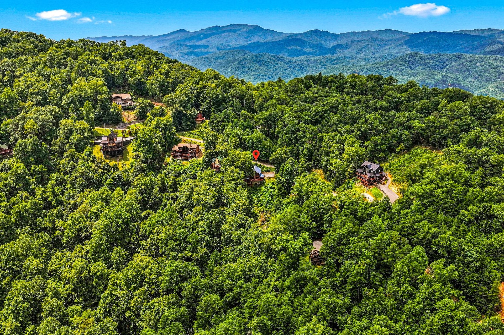 Aerial perspective of rental properties nestled among forested hills with majestic mountain ranges in the distance.