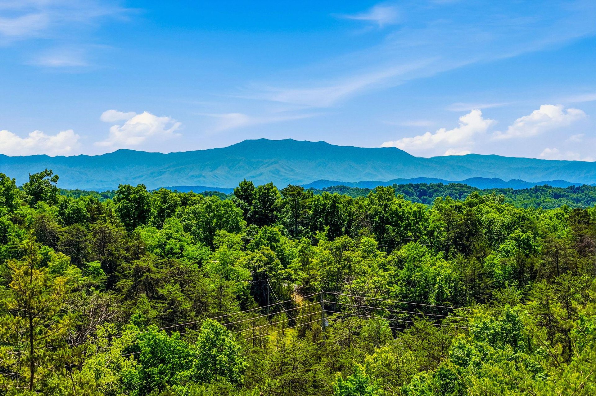 Lush green forest canopy stretches beneath dramatic mountain ridges, framing the propertys naturally stunning setting and serene location.
