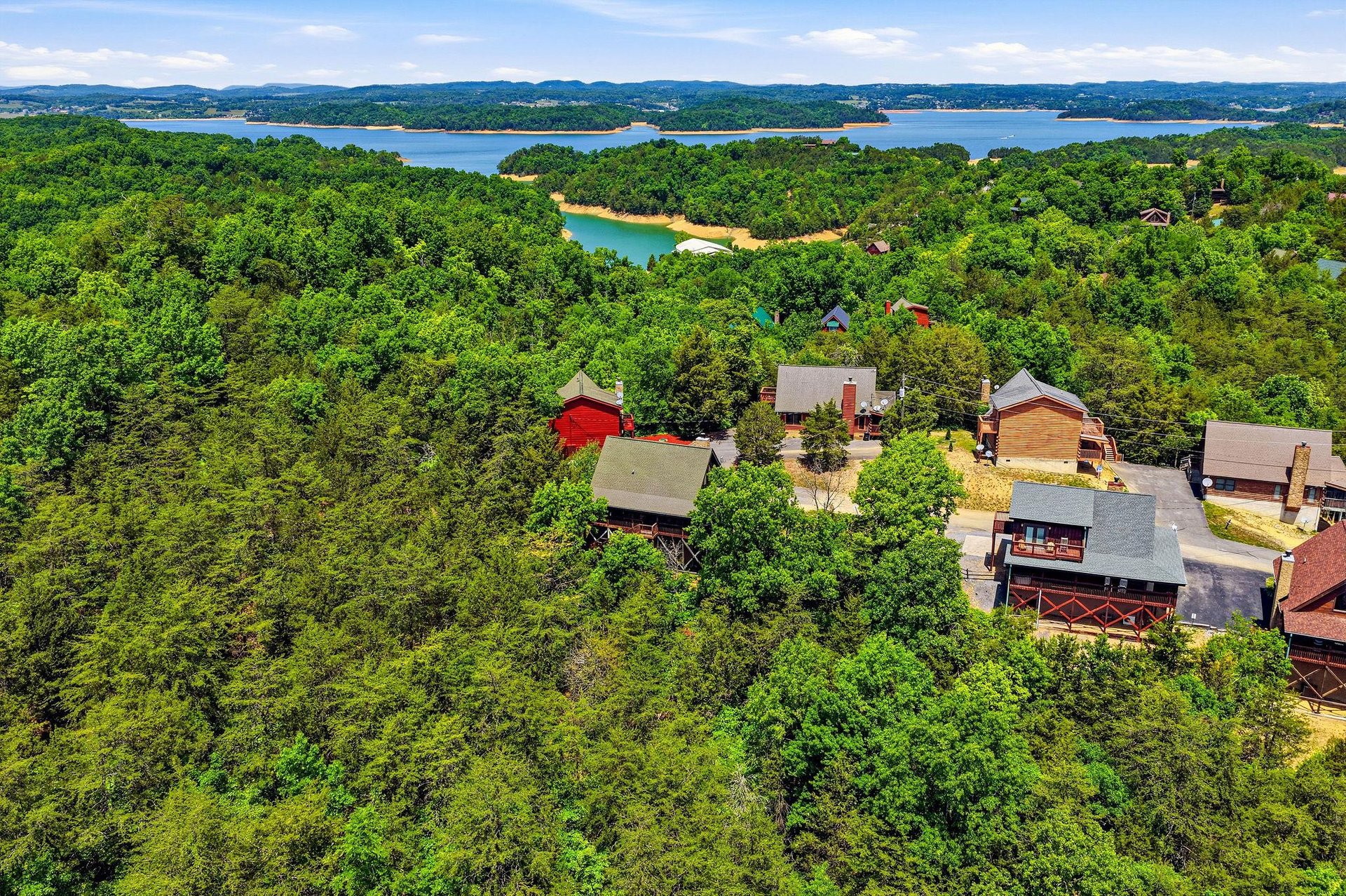 Aerial view of lakeside rental properties nestled among lush forests with stunning lake and mountain vistas in the background, offering a secluded retreat in natures embrace.