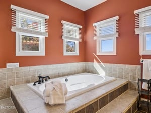 Picture yourself unwinding in this elegant soaking tub surrounded by warm terracotta walls and natural light streaming through four windows. The tiled surround and plush towels create your perfect spa