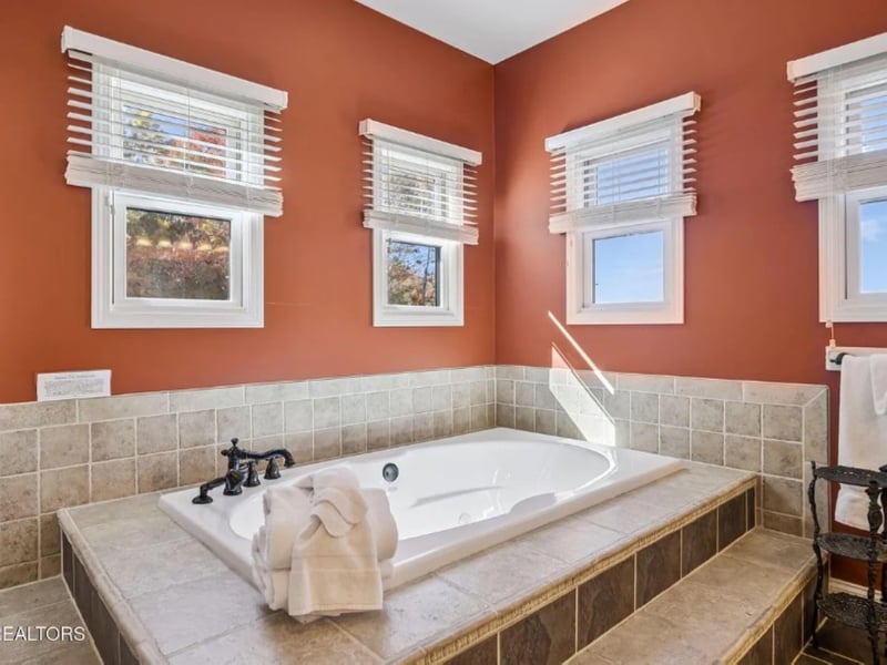 Picture yourself unwinding in this elegant soaking tub surrounded by warm terracotta walls and natural light streaming through four windows. The tiled surround and plush towels create your perfect spa