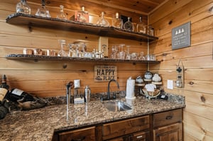 Your cabin retreat features a welcoming wet bar with granite countertops, rustic wooden shelving displaying glassware, and charming cabinthemed décor—perfect for unwinding with your favorite drink.