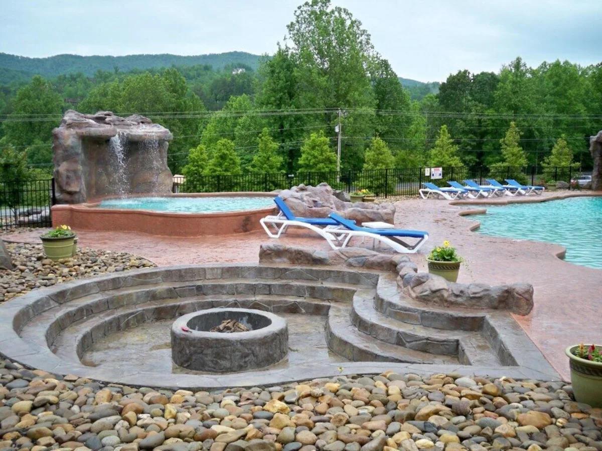 Stone firepit with tiered seating surrounded by mountain views and resortstyle pool amenities.