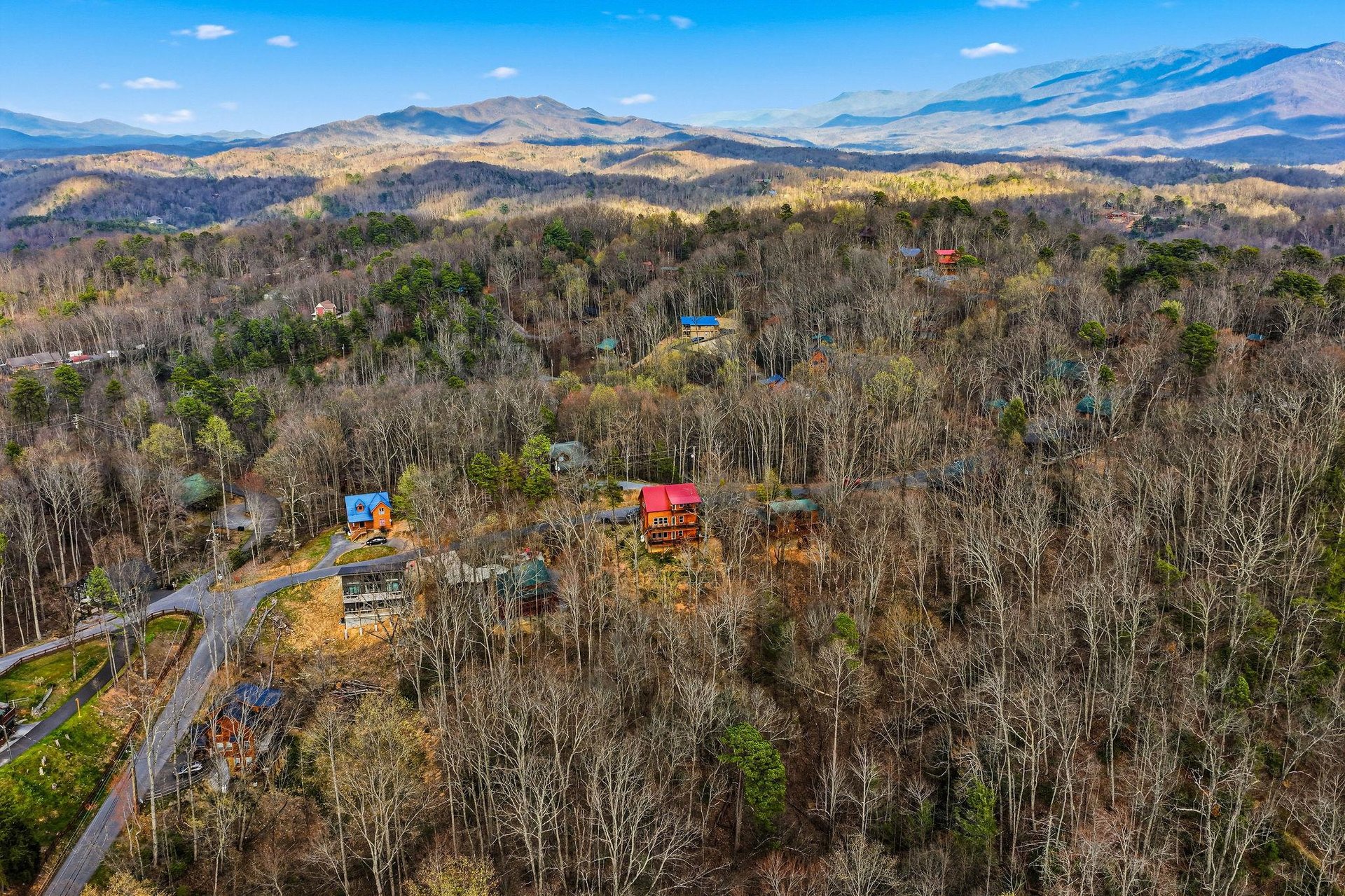 Stunning aerial view showcases mountain cabins nestled among rolling forested hills with majestic Blue Ridge peaks stretching to the horizon.