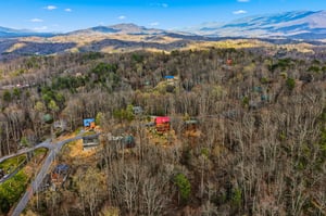 Stunning aerial view showcases mountain cabins nestled among rolling forested hills with majestic Blue Ridge peaks stretching to the horizon.