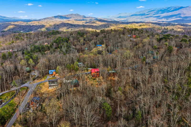 Stunning aerial view showcases mountain cabins nestled among rolling forested hills with majestic Blue Ridge peaks stretching to the horizon.