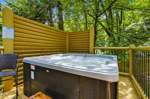 Soak away stress in your private hot tub, sheltered by golden privacy walls and surrounded by a canopy of vibrant green forest—a peaceful escape under dappled sunlight.
