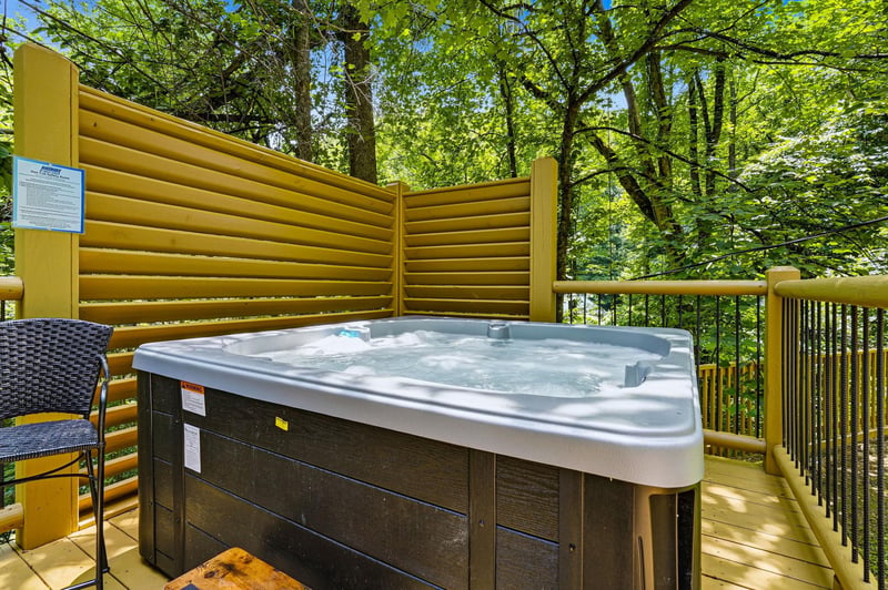 Soak away stress in your private hot tub, sheltered by golden privacy walls and surrounded by a canopy of vibrant green forest—a peaceful escape under dappled sunlight.
