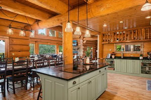Step into your rustic retreat, where warm wood surrounds you and natural light spills through large windows. Gather around the spacious kitchen island or relax at the dining table beneath charming pen