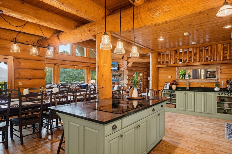 Step into your rustic retreat, where warm wood surrounds you and natural light spills through large windows. Gather around the spacious kitchen island or relax at the dining table beneath charming pen