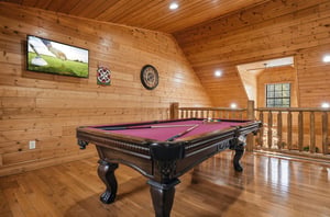 Your private game room awaits with a professional pool table, mounted TV, and warm wood finishes throughout this cozy loft space.