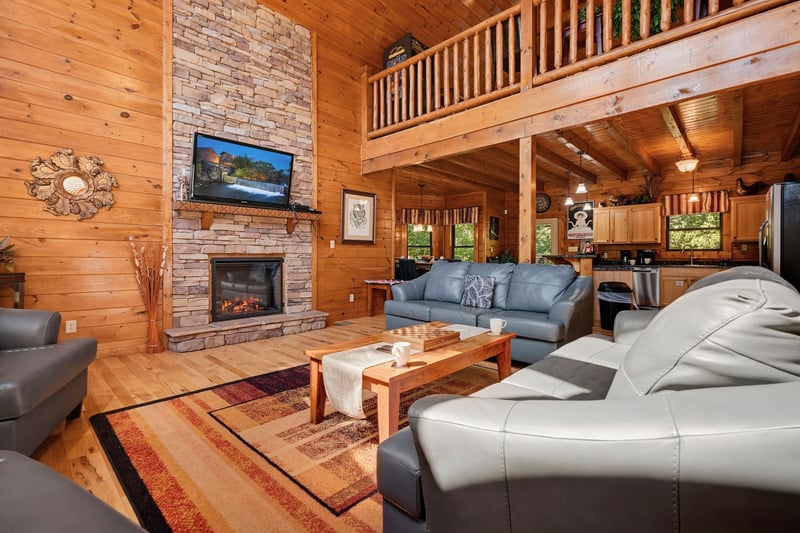 Unwind in your spacious great room with soaring ceilings, a cozy stone fireplace, and plush seating. Natural wood walls and a loft balcony create a warm mountain retreat.