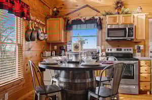 Your rustic cabin kitchen features warm wood walls, modern appliances, and charming barrel dining table perfect for intimate mountain meals.