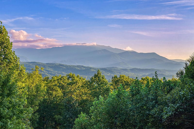 The property sits within a lush natural landscape of forested hills, with layered mountain ranges creating a peaceful backdrop during daylight hours.