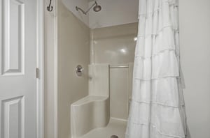 A clean, bright bathroom features a tubshower combo with dual showerheads and a crisp white curtain. Fresh towels await your arrival, ready for a refreshing rinse after a day of adventure.