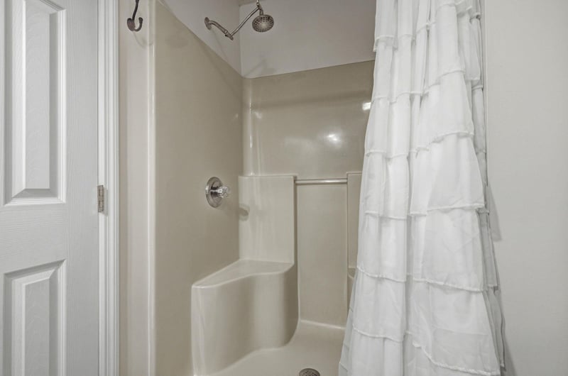 A clean, bright bathroom features a tubshower combo with dual showerheads and a crisp white curtain. Fresh towels await your arrival, ready for a refreshing rinse after a day of adventure.