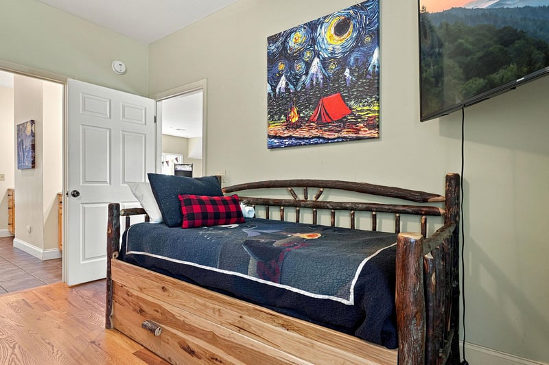 Your cozy retreat features a rustic trundle bed with charming campthemed artwork, blending mountain cabin warmth with homey comfort for a peaceful nights rest.