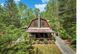 Charming log cabin nestled among towering trees, featuring a welcoming covered porch and peaceful forest setting for the perfect mountain retreat.