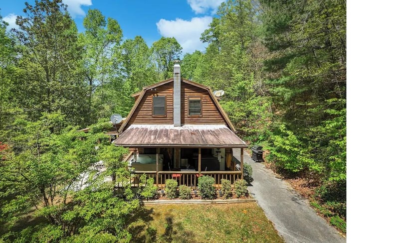 Charming log cabin nestled among towering trees, featuring a welcoming covered porch and peaceful forest setting for the perfect mountain retreat.