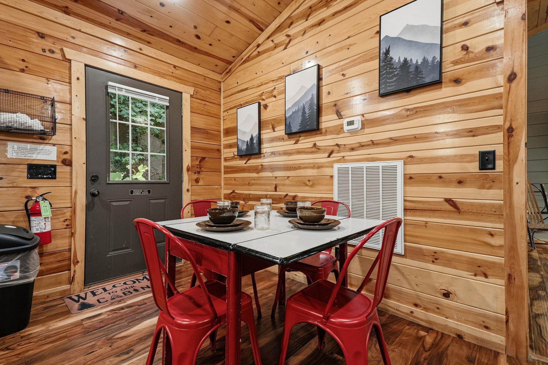 Gather around the inviting dining table in your cozy cabin, where warm wood walls and bright red chairs create the perfect setting for shared meals and great conversation.
