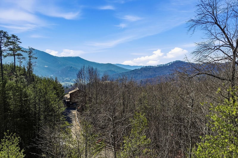 Panoramic mountain views stretch across rolling forested hills beneath a bright blue sky dotted with white clouds.