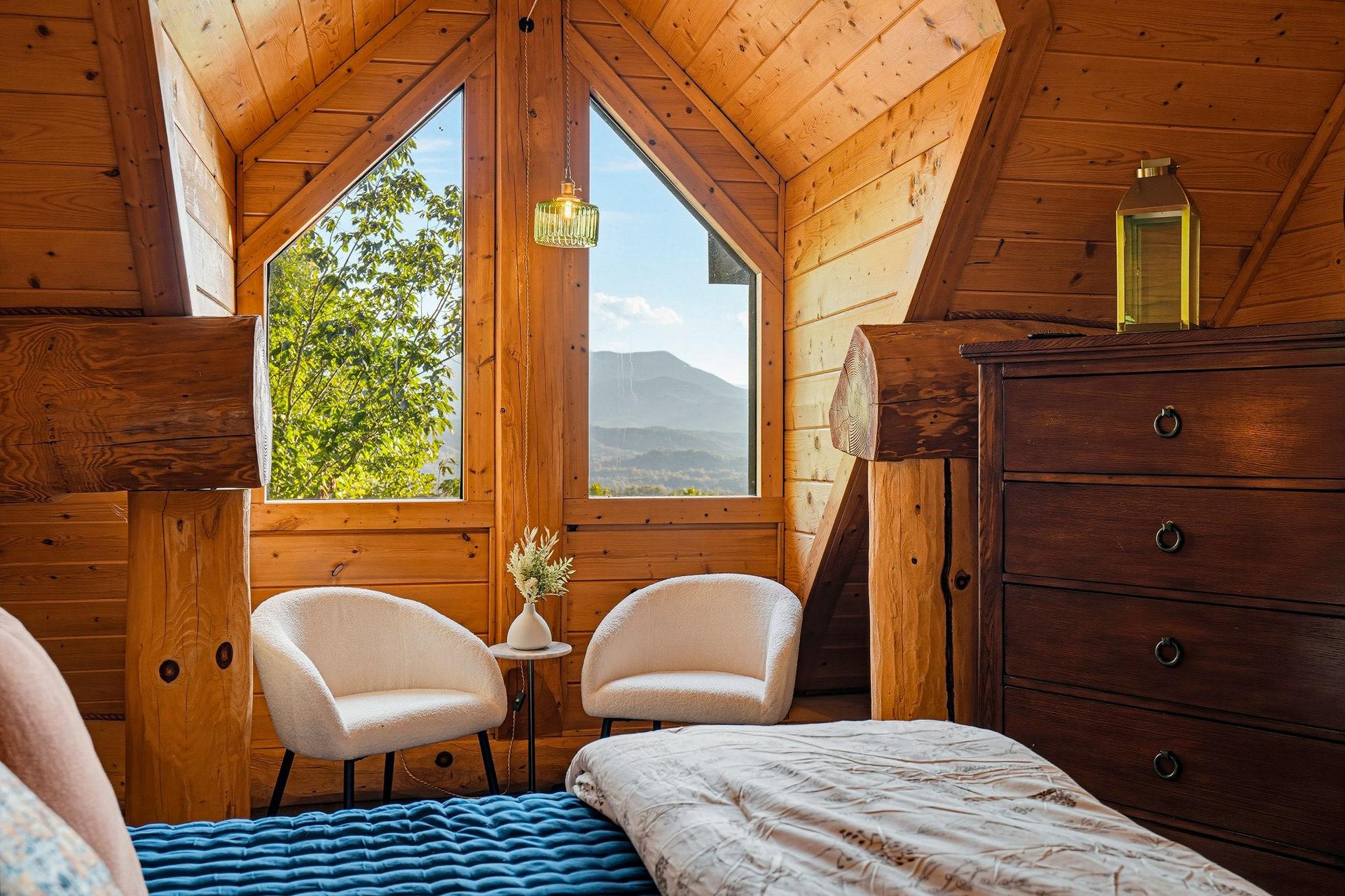 Wake up to mountain views framed by floortoceiling windows in this cozy cabin bedroom, where natural wood walls and peaceful seating invite you to start your mornings slowly.