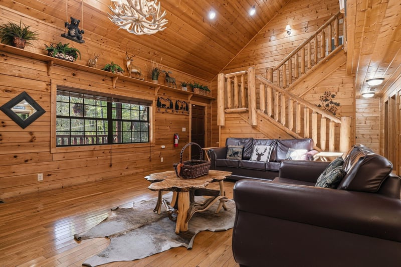 Relax in your rustic living room with leather sofas, antler chandelier, and cowhide rug creating the perfect cabin atmosphere.