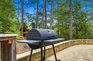 A charcoal grill awaits your cookout under towering pines, with forest views creating the perfect backdrop for outdoor dining and relaxation.