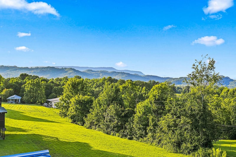 Stunning mountain vistas stretch across lush green landscapes, framed by trees and blue skies. The peaceful surroundings create an idyllic retreat setting.