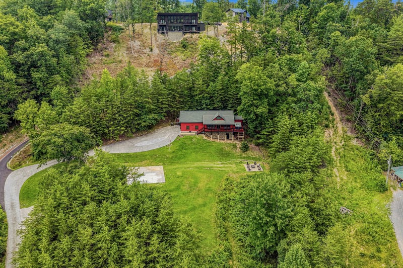 The property sits nestled in lush hillside forest, offering a serene private escape surrounded by nature. The expansive lawn and mature trees provide a peaceful mountain retreat setting.