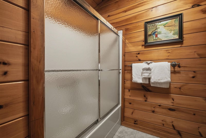 Step into your rustic bathroom with warm wood walls and a spacious glass shower where you can unwind after your mountain adventures.
