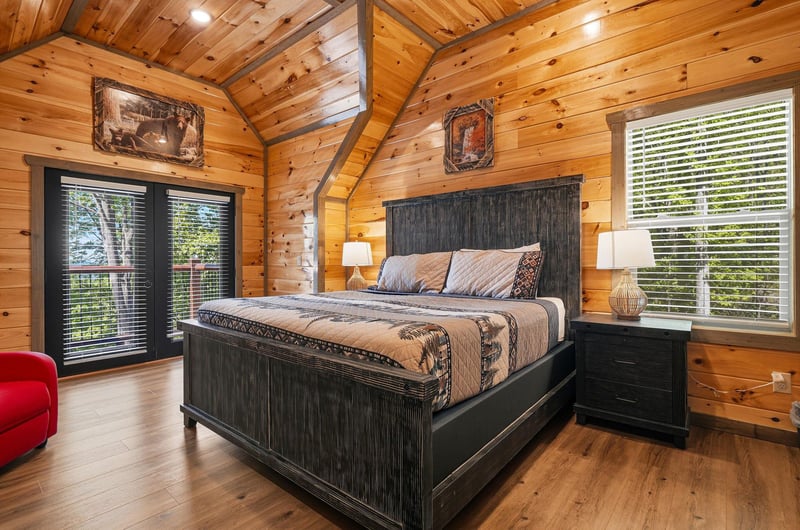 Unwind in your rustic bedroom featuring warm wood walls, cozy bedding, and peaceful forest views through large windows.