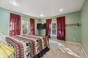 Relax in your serene, spacious bedroom with cozy green walls, charming plaid accents, a mounted TV, and peaceful views through bright windows—your perfect retreat after a day of adventure.