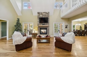 Gather in this spacious living room where vaulted ceilings and a stunning stone fireplace create your perfect retreat. Cozy sofas invite you to relax while natural light streams through French doors o